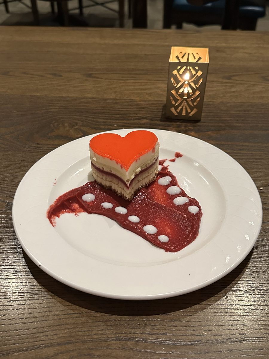 A heart-shaped layered dessert with raspberry sauce and a candle on a restaurant table