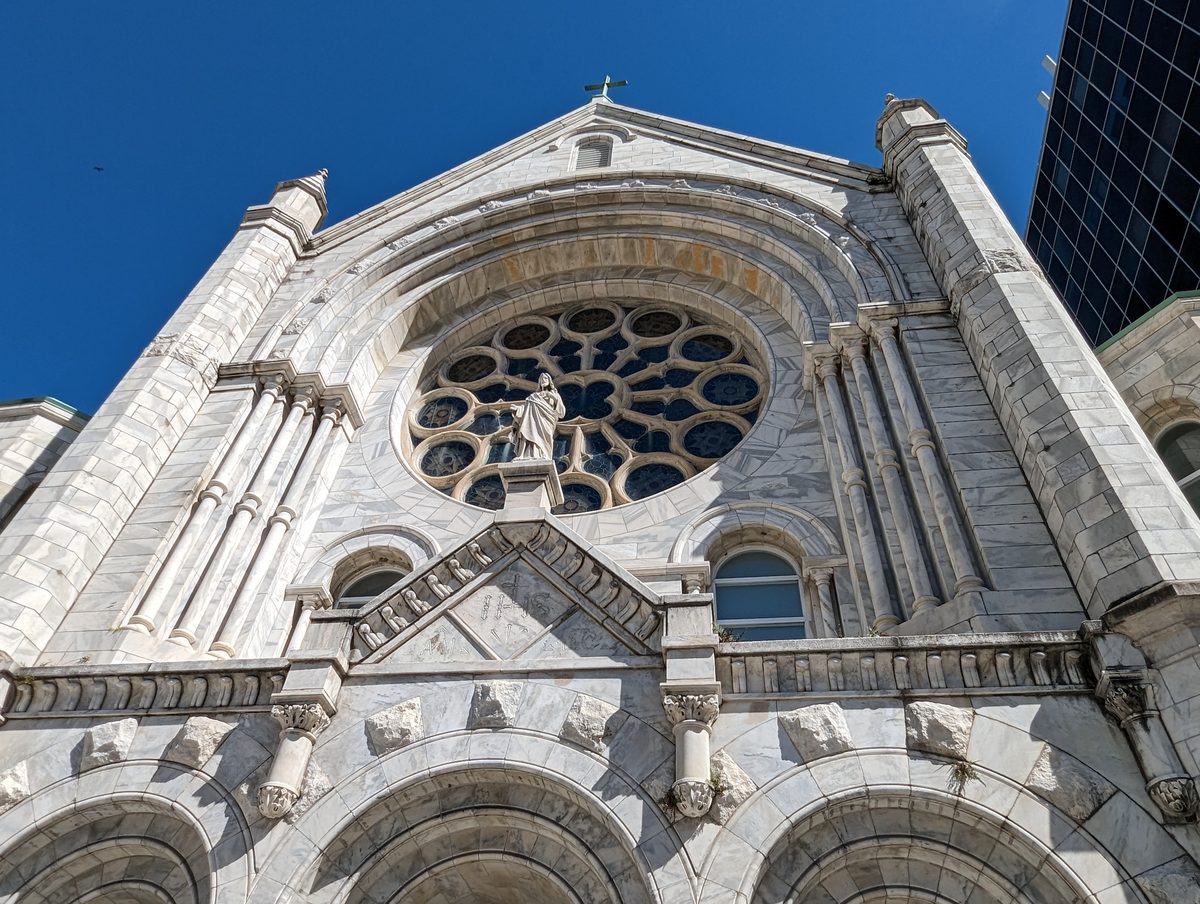 The marble facade and rose window of Sacred Heart Catholic Church against a blue sky